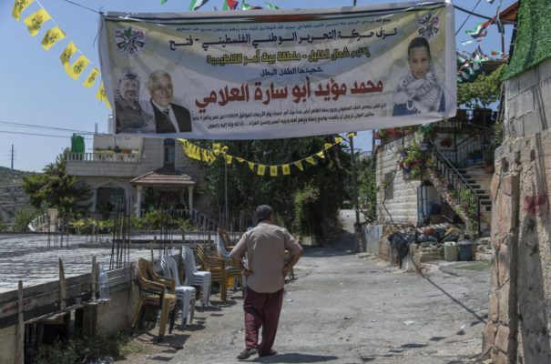 A Palestinian man passes under a banner with picture and name of slain Mohammed al-Alami, 12 and reads "Palestinian National Liberation movement, Fatah, offers her hero martyr child," infant of the family house, in the West Bank village of Beit Ummar, near Hebron, Wednesday, Aug. 4, 2021